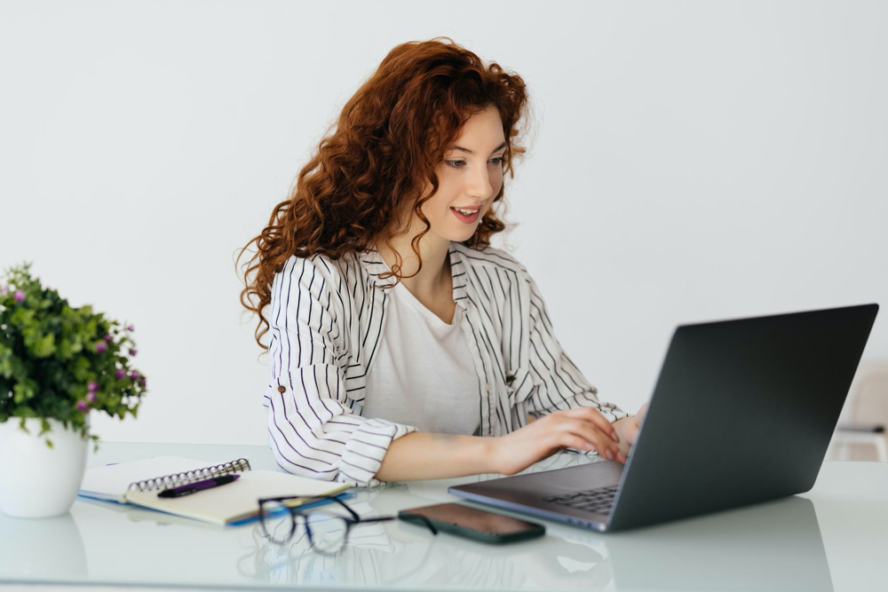 ginger woman typing on laptop while sitting at desk in home