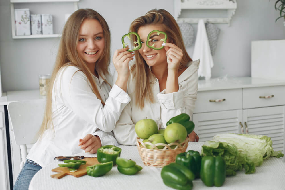 two young attractive women holding up green peppers cutting them preparing them to eat