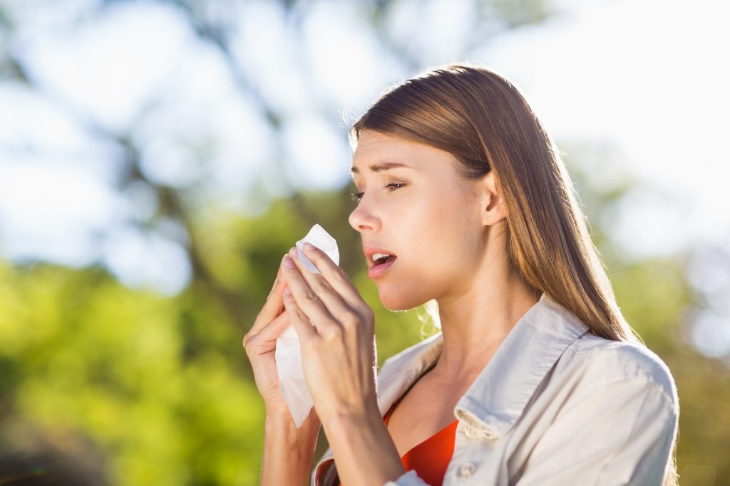 woman outside blowing her nose because she's having allergies.