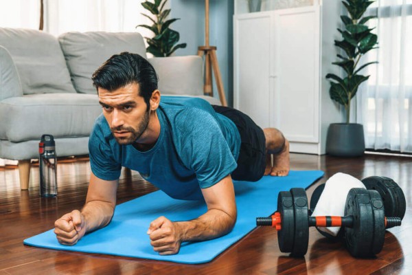 Athletic and sporty man doing plank on fitness mat at gaiety home