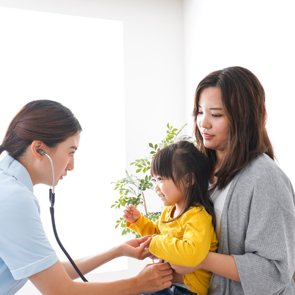 young mom holding daughter while doctor checks her lungs