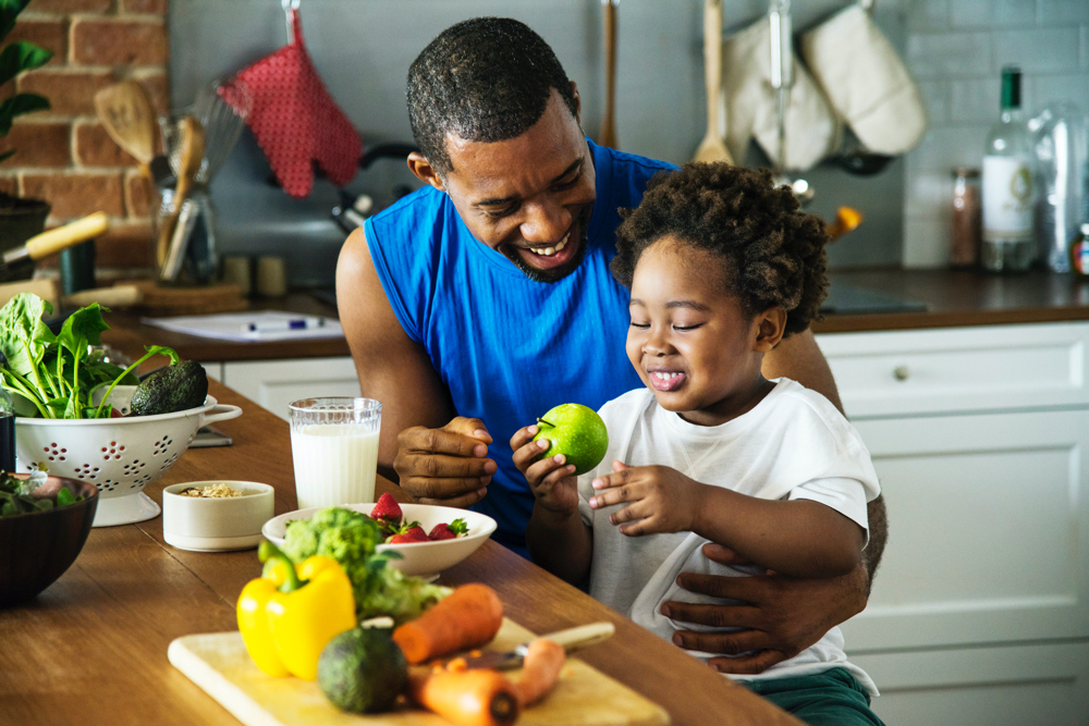 father playing with his son while in the kitchen with fruit