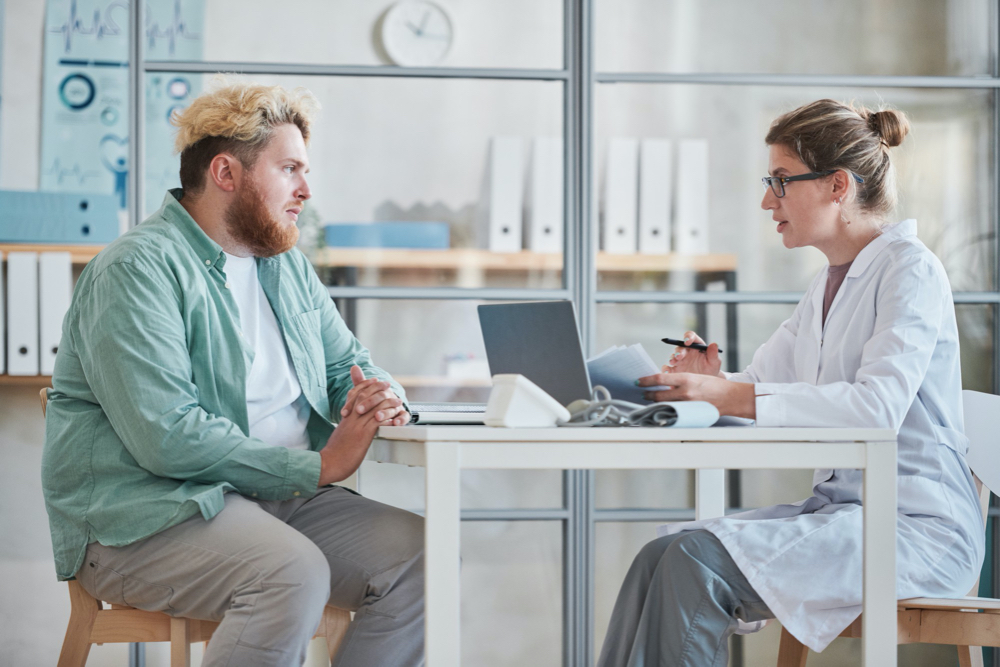 overweight man sitting at the table together with doctor and talking about his health during his visit