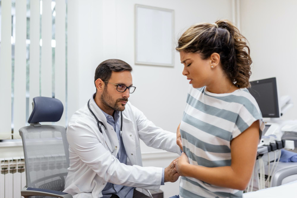 Free photo patient telling physician about her pain and health problems during visit to hospital young woman complaining about back or kidney ache while sitting on examination bed at the doctor's office
