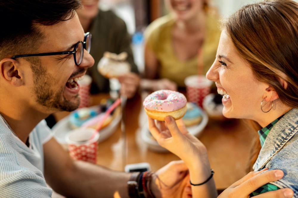 cheerful couple having fun while eating sugary donuts in a cafe