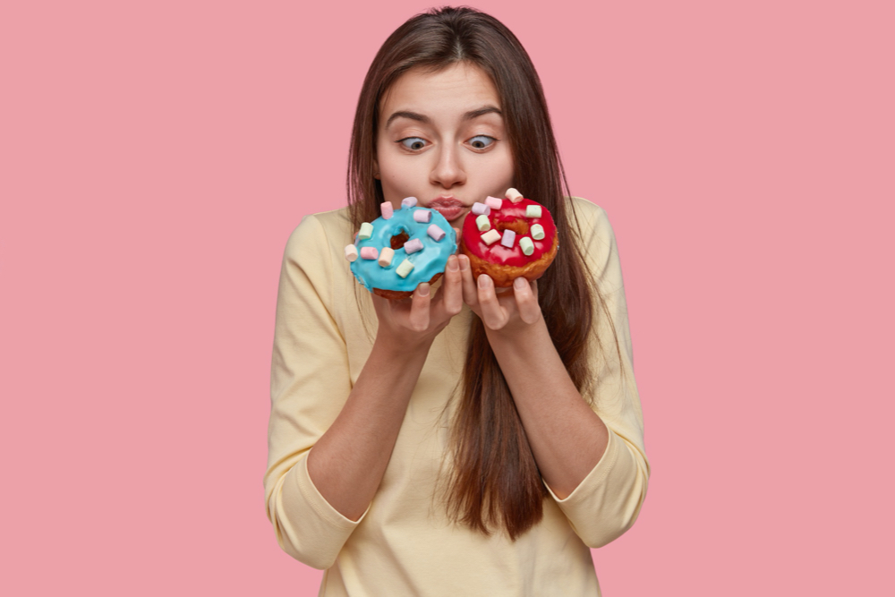 horizontal shot of shocked pretty european woman holds blue and red doughnuts