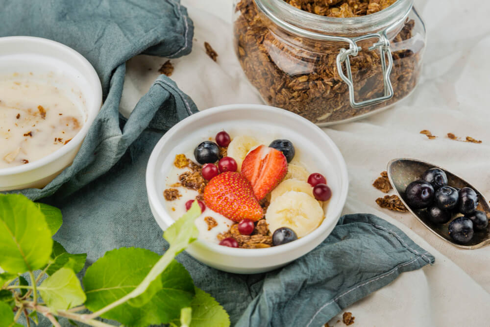 bowl on counter filled with prebiotic greek yogurt. There is strawberries, bananas, oats, granola, and blueberries on top.