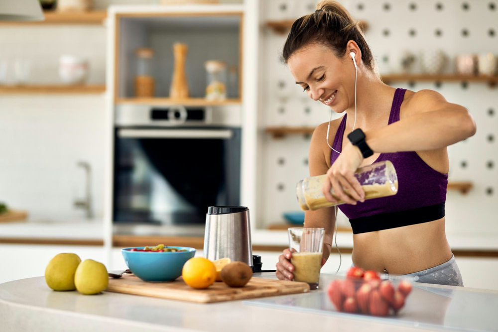 young happy athletic woman having a fruit smoothie for breakfast in the kitchen