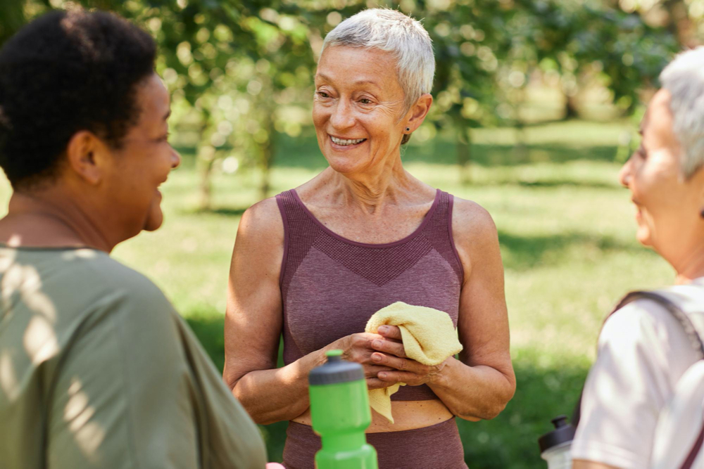 Smiling senior woman chatting with friends after outdoor workout in park