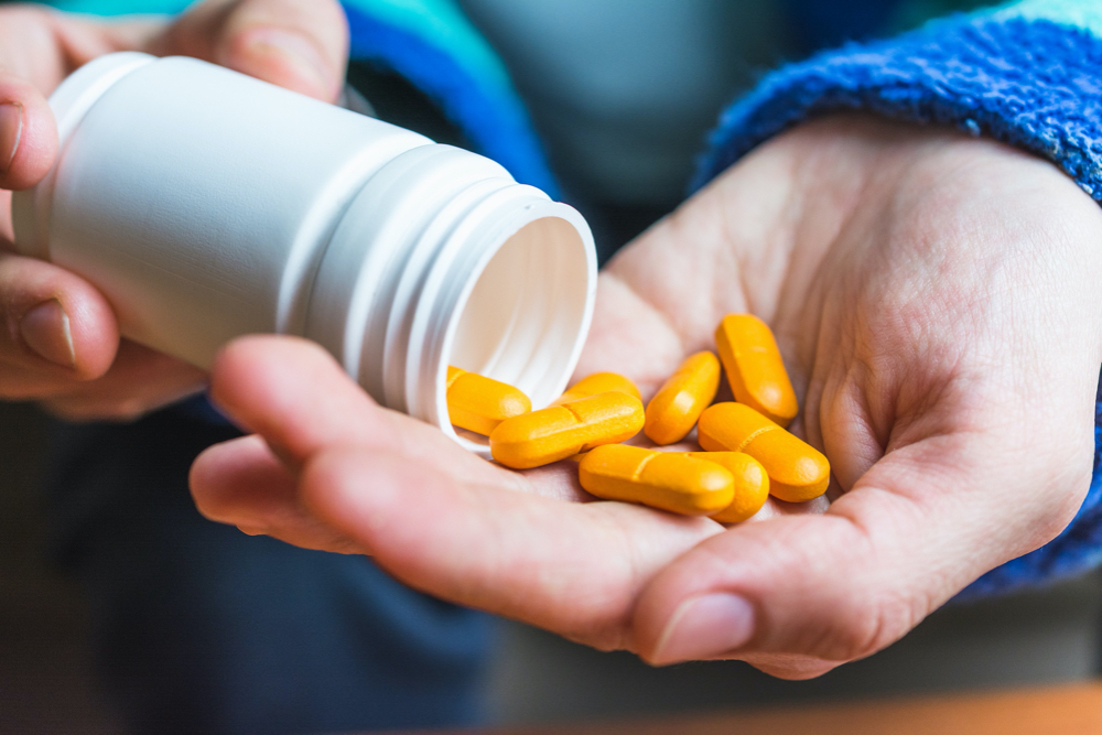 Person pouring yellow pills into his hand from a container