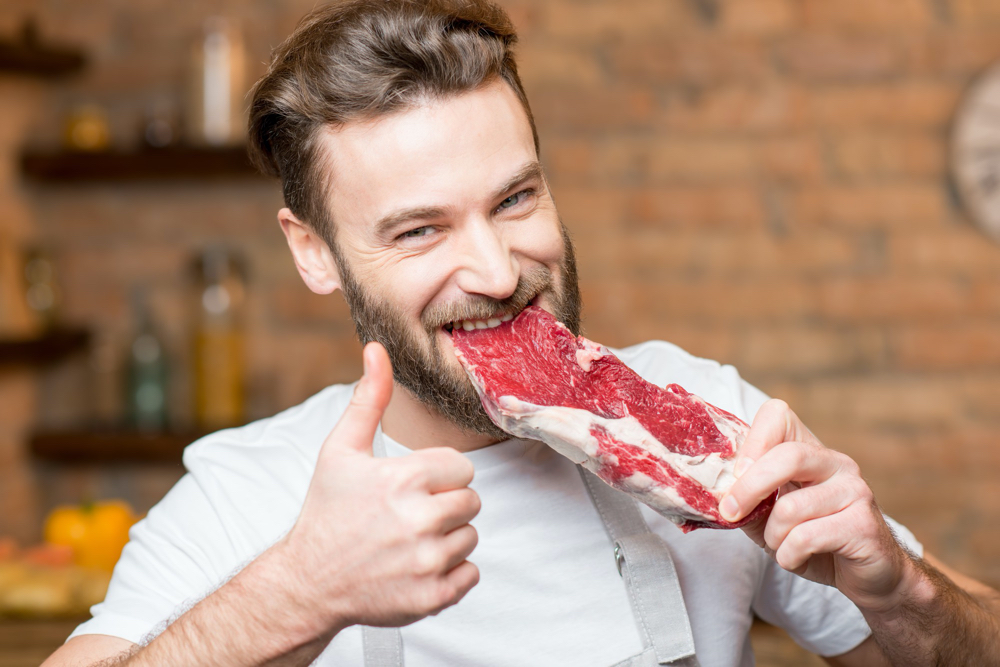 man biting raw meat on the kitchen