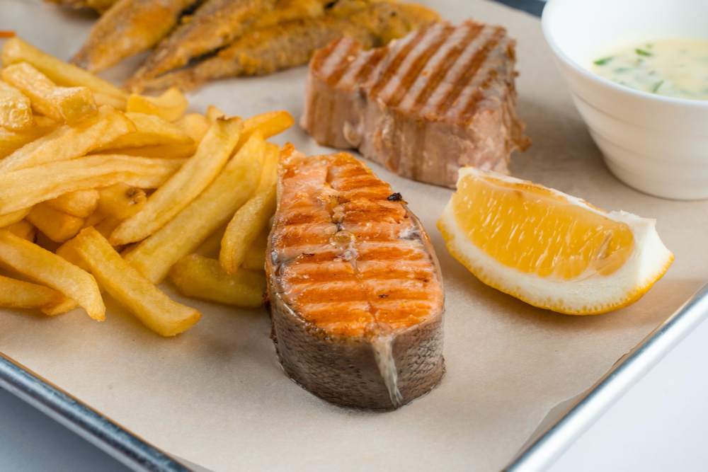 Grilled salmon steak with lemon and fries on light background.