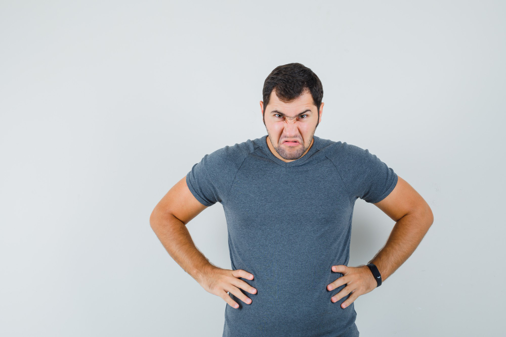 Young male holding hands on waist in grey t-shirt and looking furious