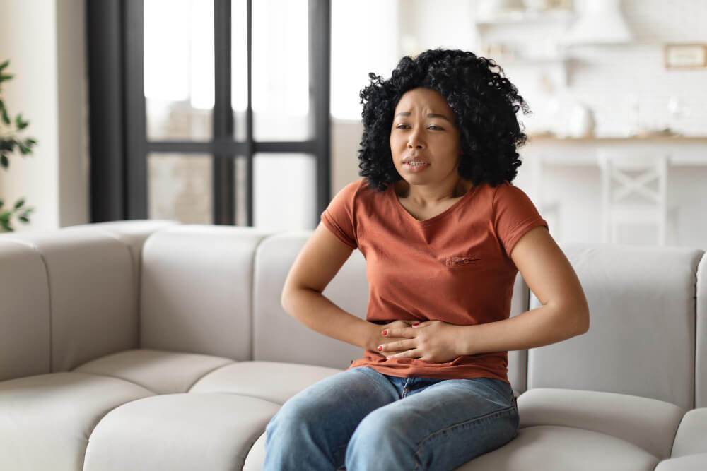 Stomach ache sick black woman suffering from acute abdominal pain at home
